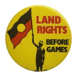 Round yellow badge with figure holding Aboriginal flag of black red and yellow. Red and black text.