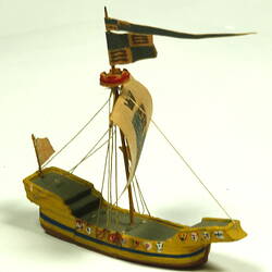 Three quarter view of ship with yellow hull and painted sail.