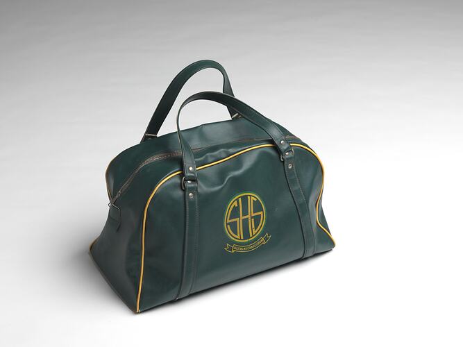 Green school bag with central zipper, two handles, yellow piping and logo on side.