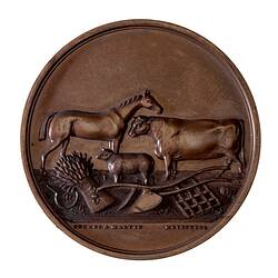 Round bronze medal with horse, sheep and bull. Below is wheat-sheaf, plough scarifier and scythe.