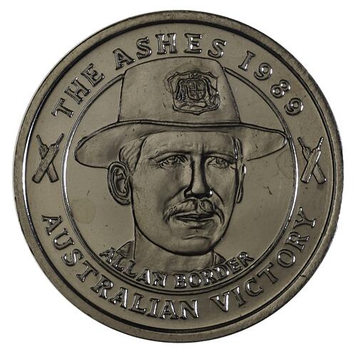 Round medal with man wearing hat and text around edge.