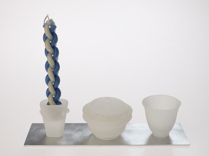 Opaque glass set on metal tray. Candle holder with woven blue white candle, lidded spice container and cup.