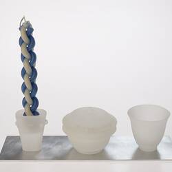 Opaque glass set on metal tray. Candle holder with woven blue white candle, lidded spice container and cup.