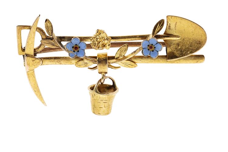 Gold brooch with horizontal pick and shovel. Gold bucket in centre. Ttwo blbue flowers.