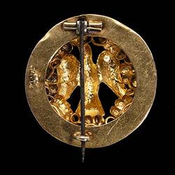 Back of round gold brooch with large bird. Vertical pin, closed.