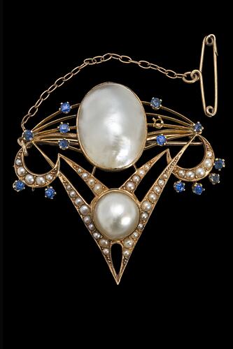 Delicate gold inverted triangle brooch with two main pearls framed by seed pearls and blue paste. A fine gold chain and pin extend from top left corner.