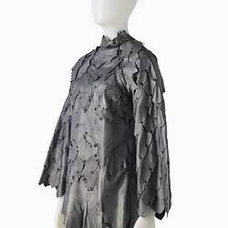 Short shift-style dress made from irregular pieces of pewter grey leather to resemble reptilian scales. Left three quarter view.