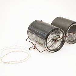 Two metal tins with lids. Bound together with wire. Cord at one end to pull them along.