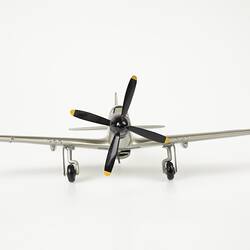 Wood model plane painted silver. Front black four blade propeller. Three wheels.