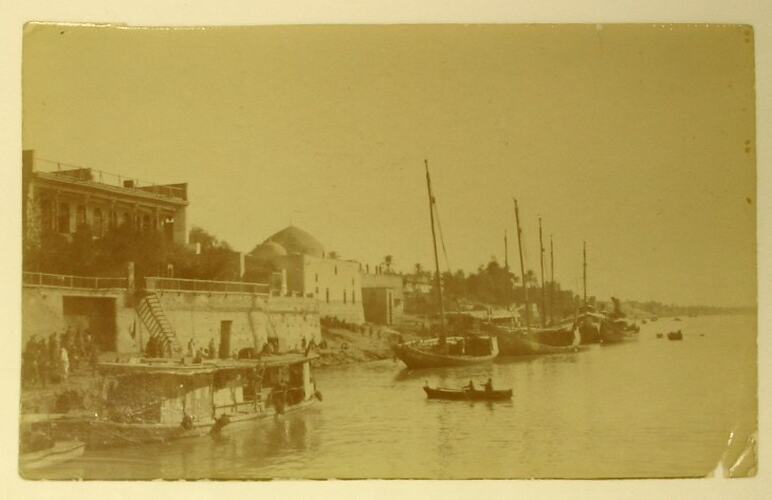 River front with buildings, sail boats and people in row boat.