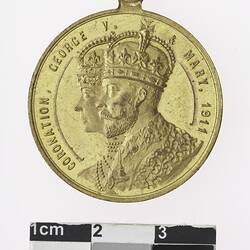 Round gold coloured medal with profile of crowned man and woman and text surrounding.