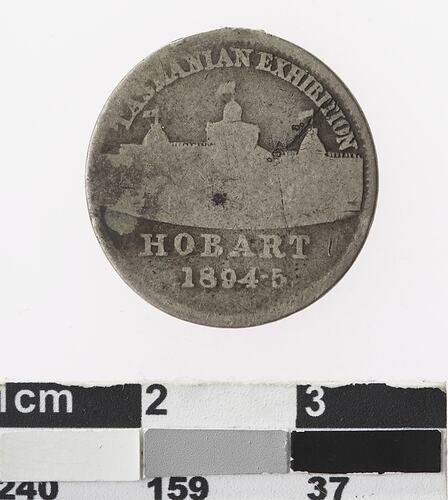 Round silver coloured medal with building, text above and below.