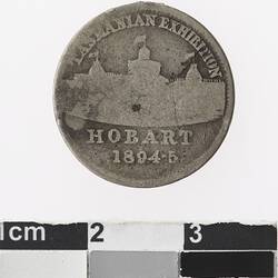 Round silver coloured medal with building, text above and below.