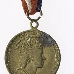 Round medal with profile of crowned woman and text surrounding, with red, white and blue ribbon.