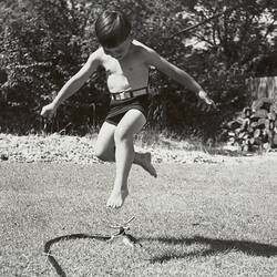 Boy Jumping Over Rotating Sprinkler, Backyard, Blackburn, 1953