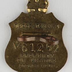 Shield shaped metal badge with inscribed text.