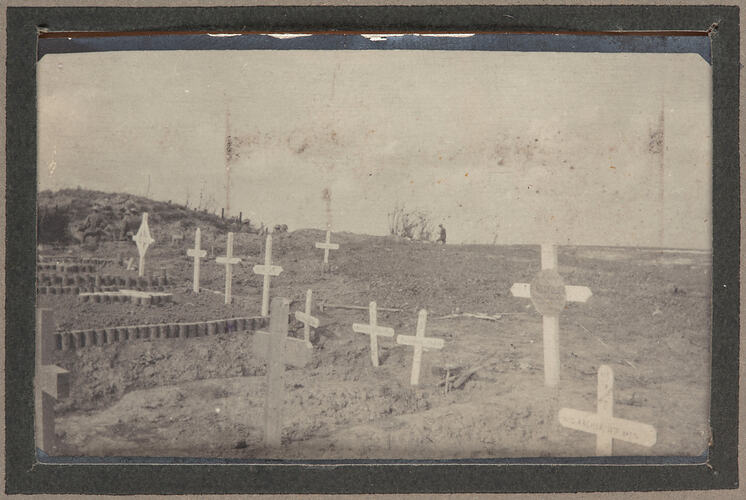 Graveyard in dirt with cross shaped markers, with service men in background.
