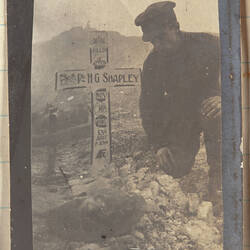 Soldier kneeling next to grave marked with white cross.