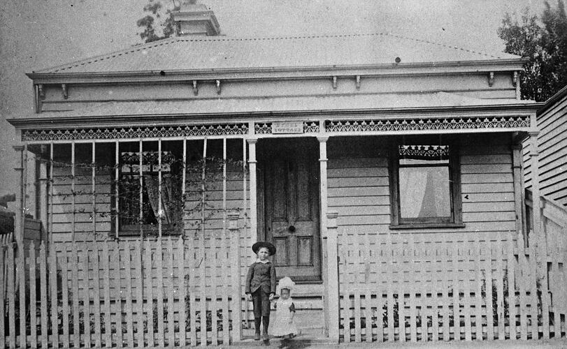 A young boy and a small girl standing at the gate of a small house