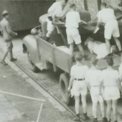 A group of men loading two bodies wrapped in cloth into the back of a truck.
