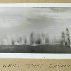 Multiple explosions rising from the ocean in middleground, group of plains in left background.