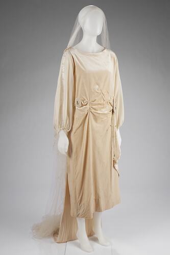 Long-sleeved cream dress, hip brooch, and fine-netted veil.