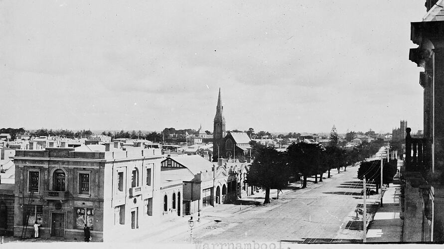 View looking along a town street. A church with steeple is midway on the left.