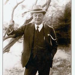Man wearing suit, posed with tree.