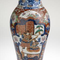 Ornate colourful vase, slightly tapered body with a small lip. Off-white base with two Shogun figures amongst peonies, cherry blossoms, chrysanthemums, fans and butterflies.