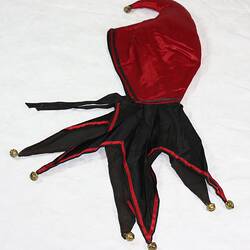 Red and black jester's hat. The peaked cap is red and collar section black. Each peak has a bell.