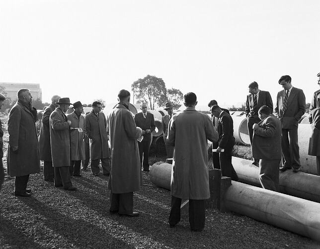 Monochrome photograph of men testing cement pipes.