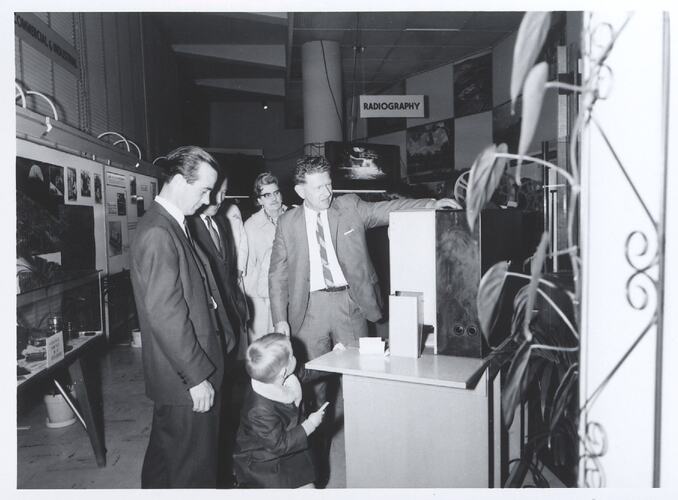 Group watching a man gesturing to large machine.