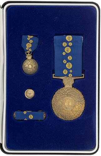 Two medals, one badge and one ribbon in blue fabric lined medal box.