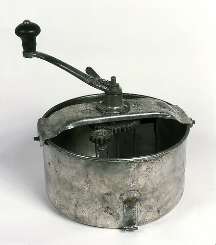 Metal mixing bowl with crank handle attached.