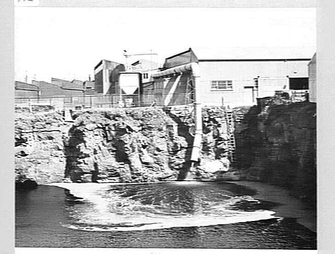 Industrial building with waste pipe into flooded quarry.