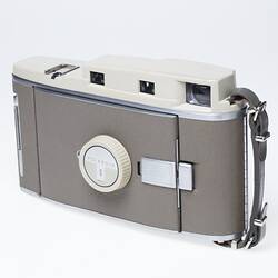 Off-white camera, taupe cover, metal trim. Closed front view.