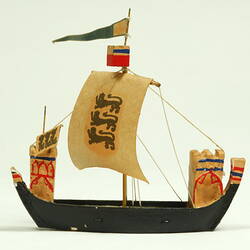 Side view of ship with black hull and painted sail.