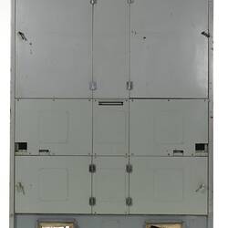 Grey metal cabinet, four closed doors. Two vent holes at base with wires visible.