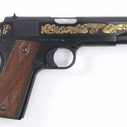Pistol with brown handle. Black barrel has gold decorative scrollwork and lettering.