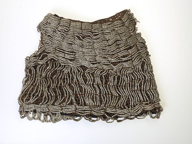 Off-white seeds thread onto bark fibre making a vest-like garment.
