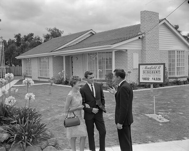 Man with male and female couple in front of house.