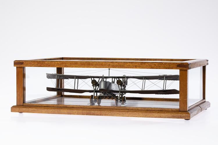 Model of a bi-plane made mostly of aluminium sheet metal. It has two pairs of wheels at front. In display case