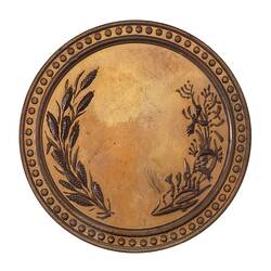 Round silver medal with no engraving framed by wheat on left and native flora on right. Decorative edge.