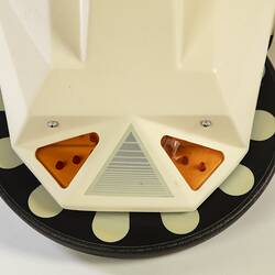 Detail of base of cream plastic robot with angular human-like shape, ie. head, shoulders, waist and legs. Black plastic features.
