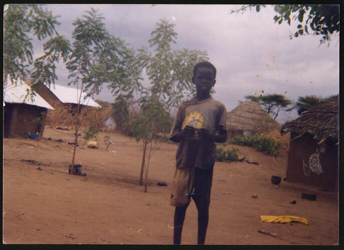 Boy standing in front of several huts.