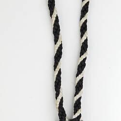 Back of triangular medal with black and white twined cord. Raised text.
