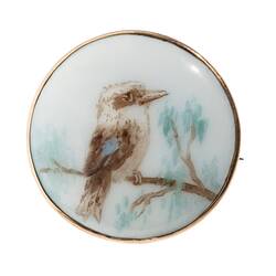 Round white porcelain brooch with hand painted kookaburra in a tree facing right.