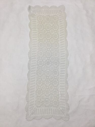 White cotton crochet table runner with scalloped edges.