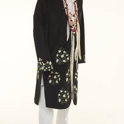 Black coat with white floral detail over white chinos pants. Long beaded necklaces.