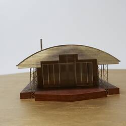 Model of a house with an arched roof, corrugated iron and wide expanses of glass.